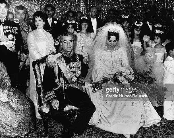 The Shah of Iran sits with his new wife the Empress Farah of Iran. The ceremony took place in the Hall of Mirrors, with the bride wearing a dress of...
