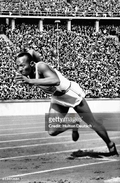 Jesse Owens leaps from the starting line during the 1936 Olympic Games in Berlin, with a crowd watching from the grandstand.