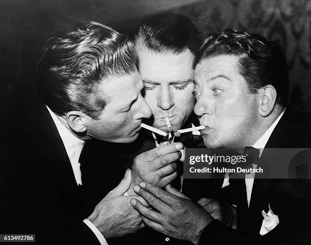 Actors Danny Kaye , Laurence Olivier and Sid Field lighting a cigarette from a single match at the Cafe de Paris in London, ca. 1950's.