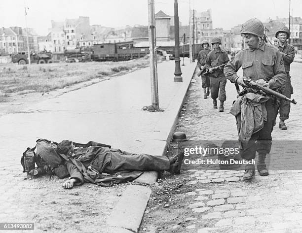 American soldiers pass by the body of a dead German soldier at the side of the road in Cherbourg, 1944.