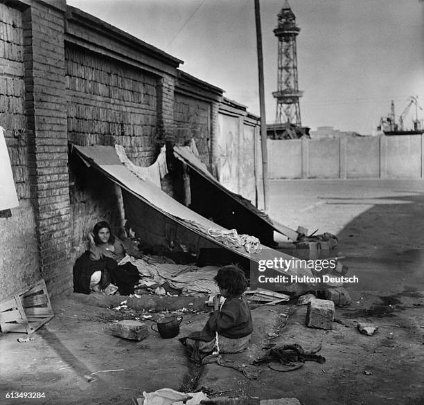 Homeless Spanish woman with tuberculosis shelters beneath a makeshift canvas canopy her husband has errected for her, Barcelona, 1951. | Location:...