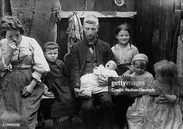 Poverty-stricken couple with their five children, the man holds a bunch of pawn tickets in his hand.