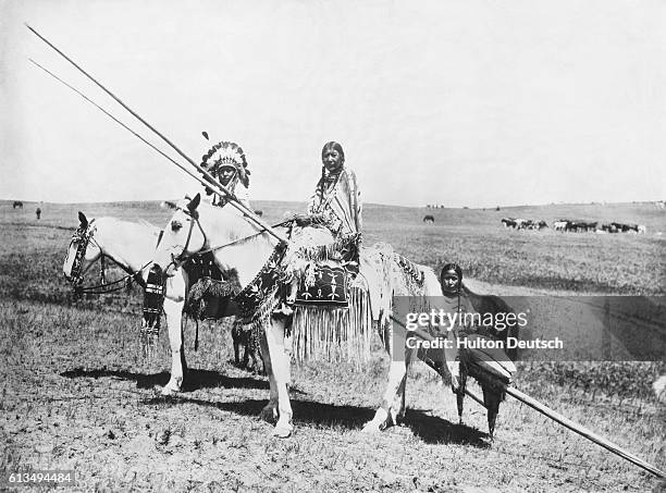 Young woman rides on a litter hauled by a horse ridden by the wife of a Native American Blackfoot chief.