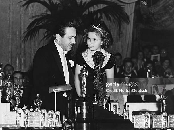 Child star Shirley Temple presents the American animator and producer, Walt Disney , with an Oscar and seven miniature statuettes, for his first...