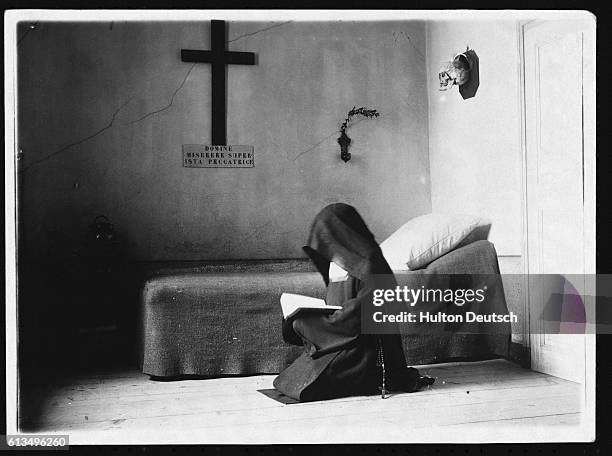 Carmelite nun kneels beside a bed, and reads a book.