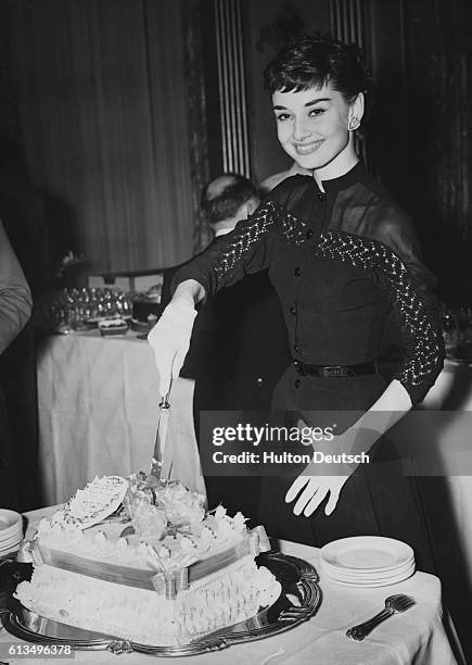 Audrey Hepburn cuts a cake at a reception in her honor at London's Claridges Hotel. | Location: Claridges Hotel, London, England.