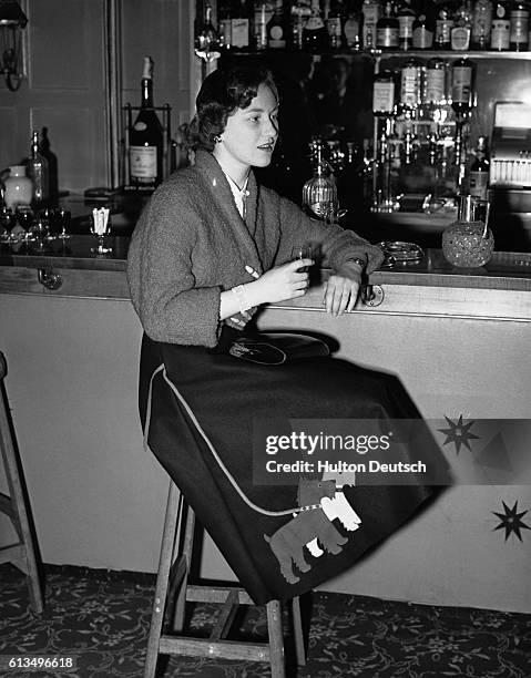 Jennifer Hill relaxes with a drink in the bar of the Bear Hotel. She wears a black felt skirt, decorated with two appliques felt dogs, and a short,...
