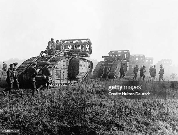 British tanks with trench-crossing equipment, advance with troops in support, during trench warfare in France during the First World War.