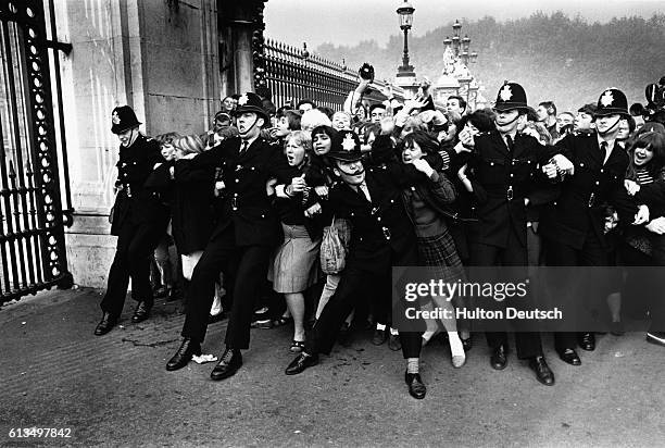 Crowd of excited fans rush against a line of police officers at the gates of Buckingham Palace, in hopes of a glimpse of the 1960s rock supergroup,...
