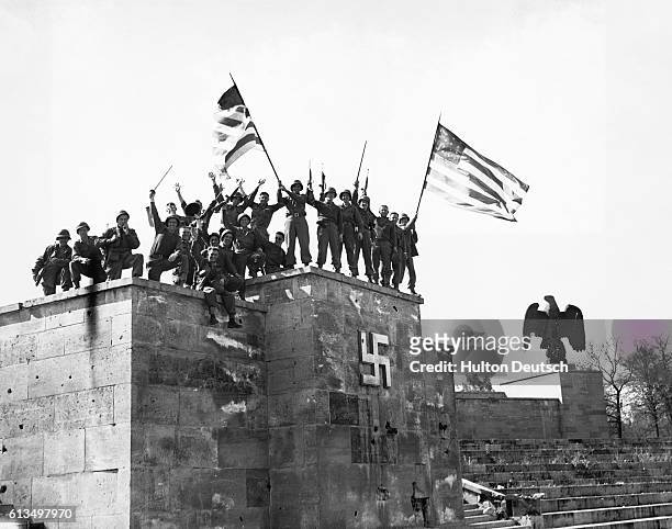 American 7th Army troops wave flags of victory on May 8, 1945 atop what was once Hitler's rostrum at the Luitpold Arena in Nuremberg, Germany....