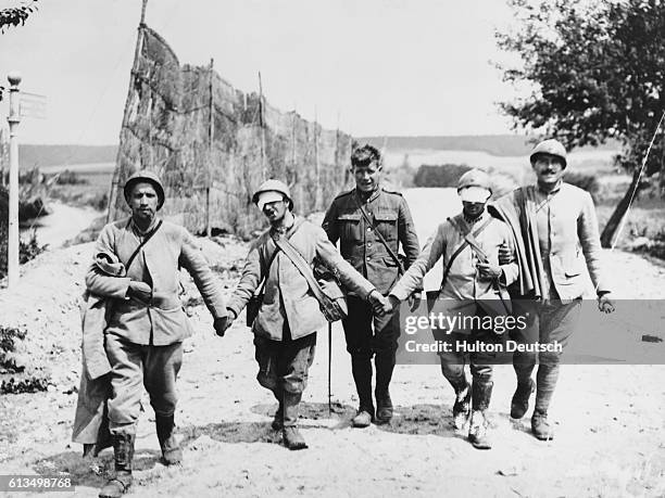 French infantrymen, blinded probably by gassing, are escorted by a British soldier after the second battle of the Marne.