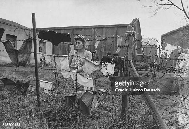 Woman refugee hangs her washing on a barbed wire fence at the building that was once a large film studio built by Mussolini. After the Liberation of...