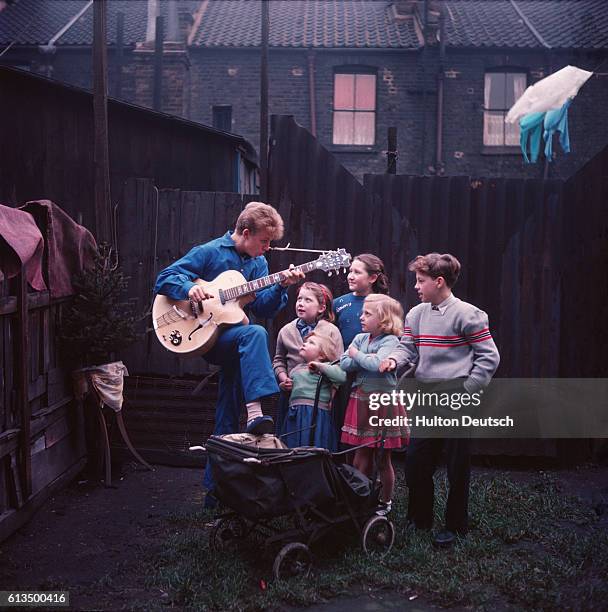 Tommy Steele, a British entertainer, plays the guitar for five children.