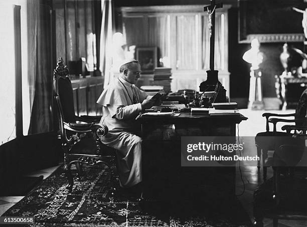 Pope Pius XI sits at a desk and reads. He was born in 1857 and died in 1939, and was Pope from 1922.