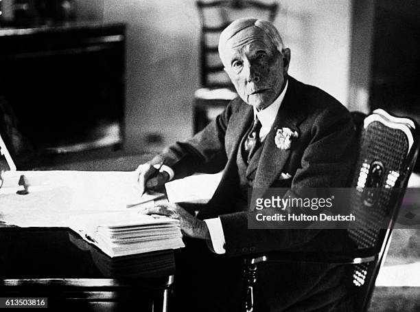 John Davidson Rockefeller , the American oil magnate and philanthropist sits writing at his desk.