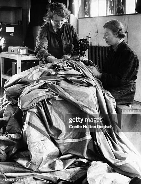 Members of the Women's Auxiliary Air Force repair a deflated weather balloon using an electric sewing machine during World War Two.