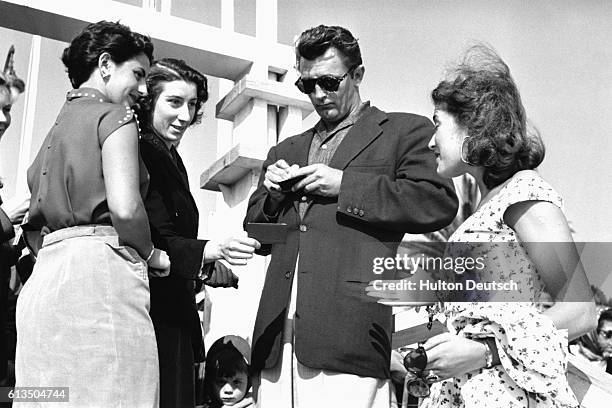 American actor Robert Mitchum signing autographs while on the French Riviera with Lise Bourdin, 1954.