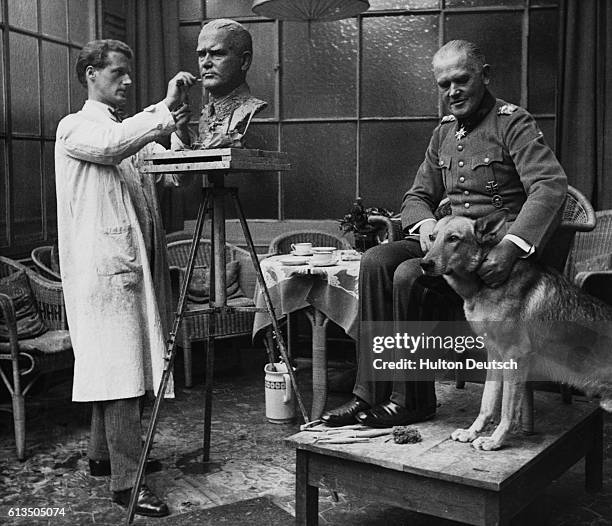 General Werner von Blomberg, the Third Reich's Minister of War, fusses over a German shepherd dog as he poses for the Swedish sculptor, Adh Hedblom.