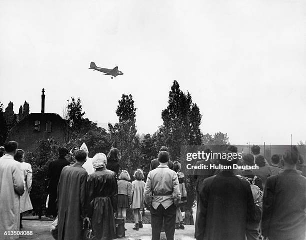 Group of Berliners by Tempelhof Airfield watches with anticipation as one of the United States C-47 Skytrain cargo planes descends from the sky...