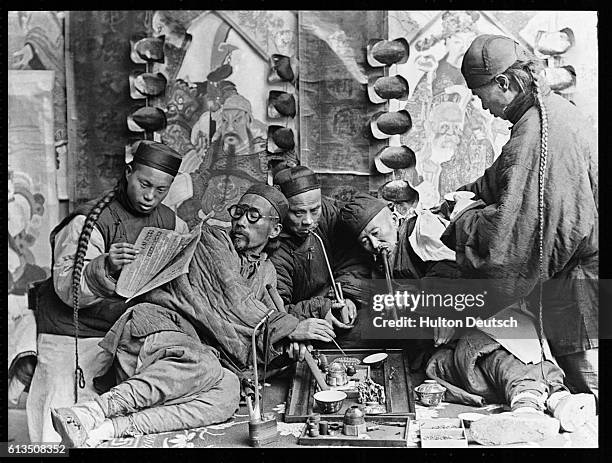 Men smoke pipes and read as they relax inside a Chinese opium den.