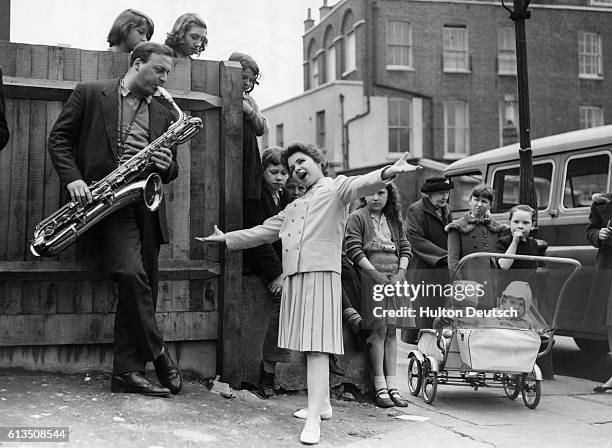 American teenage singer Brenda Lee rehearses for ITV's show Oh Boy in the streets of Islington. Watched by some of the local children.