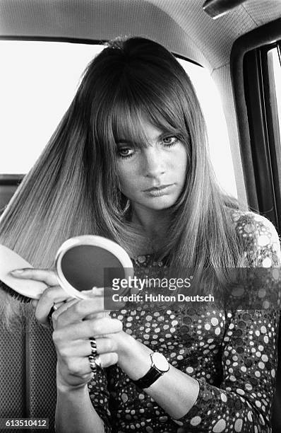 The fashion model Jean Shrimpton brushes her hair whilst in a car, 1966.