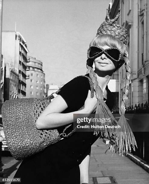 Ginette Heldman models a red, raffia, pillbox hat, with attached pigtails, sunglasses and a shoulder bag, from the spring and summer collection by...