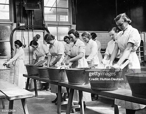 Women use washboards and tubs to clean clothes at a laundry facility.