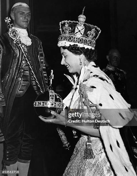 Queen Elizabeth II, wearing the Imperial State Crown and carrying the Orb, arrives at Buckingham Palace from Westminster Abbey, after her coronation...