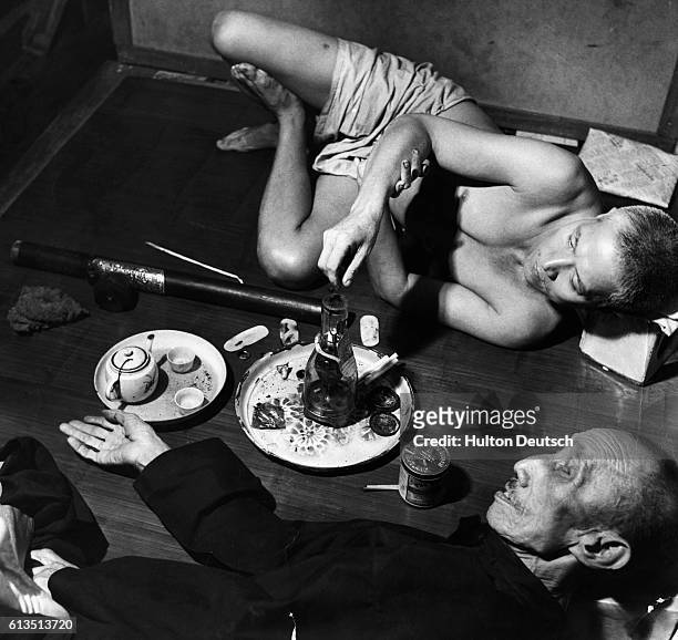 An attendant heats a blob of opium over a flame while a customer waits, in an opium den in Bangkok's Chinese quarter.