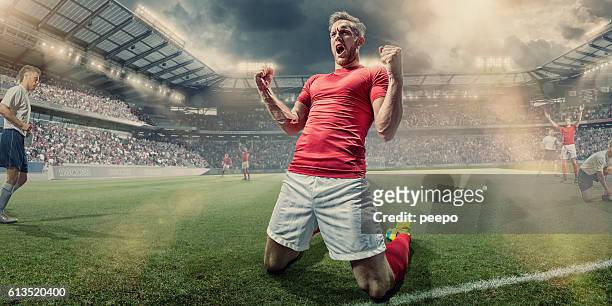 calciatore inginocchiato in campo con pugni stretti in festa - divisa sportiva foto e immagini stock