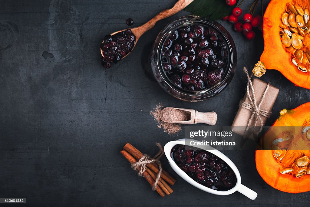 Cranberry sauce,  halved fresh pumpkin and  cinnamon sticks on grey background with  copyspace for healthy seasonal autumn cuisine. Thanksgiving concept