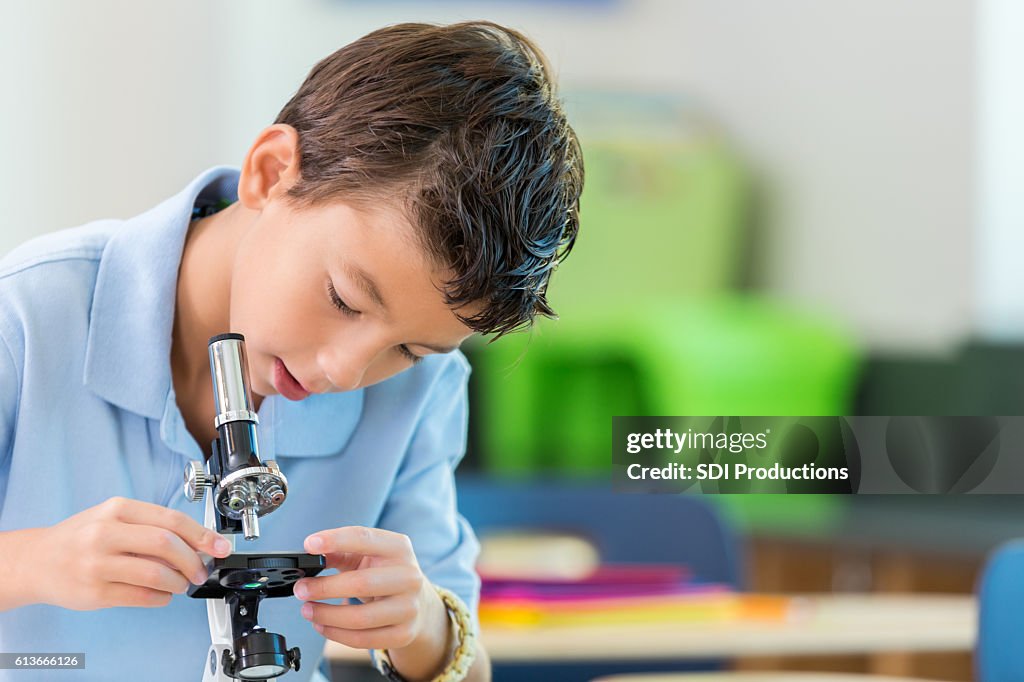 Private schoolboy concentrates while looking through microscope