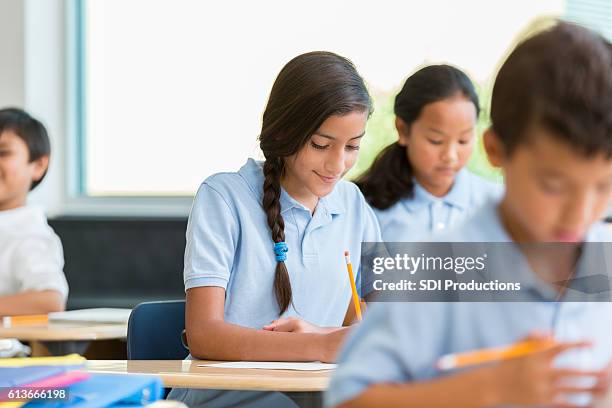 la colegiala hispana se concentra mientras trabaja en tareas de clase - uniforme fotografías e imágenes de stock