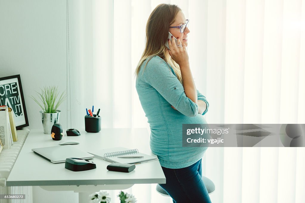Pregnant Businesswoman Talking On The Phone In Her Home Office.