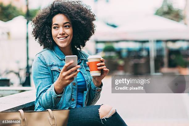 smiling woman with smart phone and coffee cup - creole ethnicity stockfoto's en -beelden