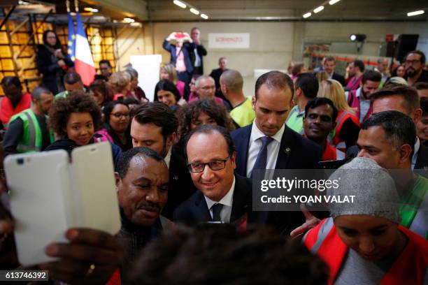 French President Francois Hollande poses with employees for selfies pictures as he visits the logistics center of Sarenza in Reau, near Paris, on...