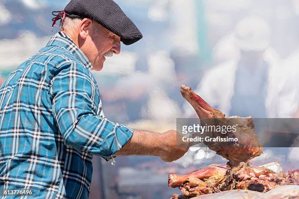 asado argentino (barbacoa) viejo gaucho controlando haunch de cabra - carne asada fotografías e imágenes de stock