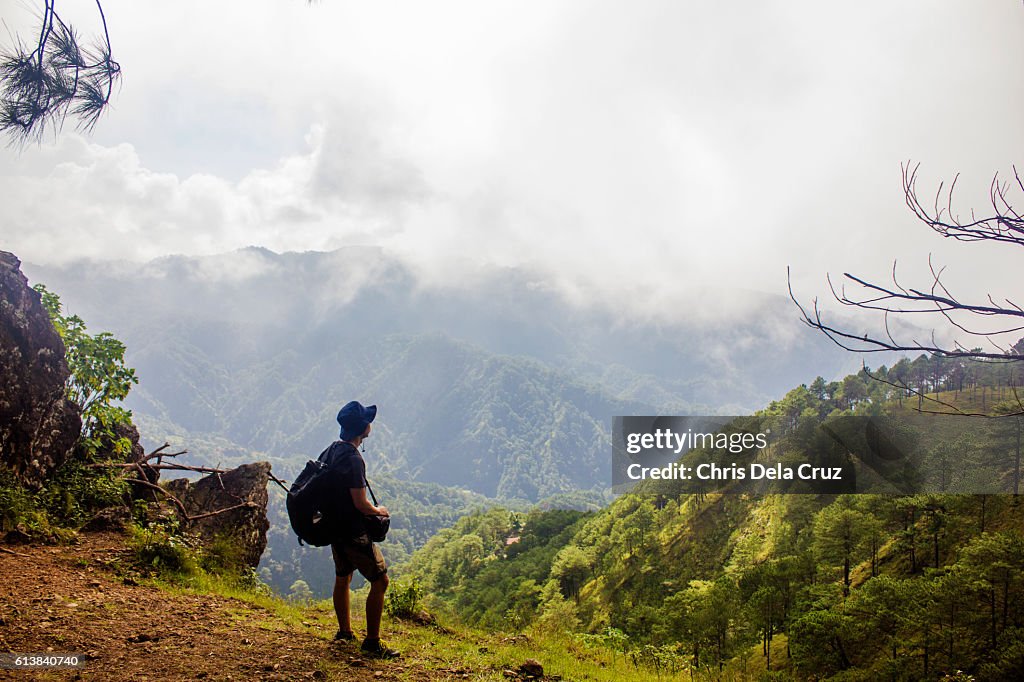 Man on top of a mountain with warm trees and cloudy sky
