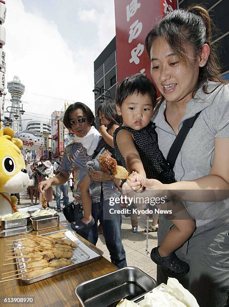 Japan - A woman and her child pick up "kushikatsu," skewered pork cutlets, in the Shinsekai district in Osaka's Naniwa Ward on Sept. 4, 2012. One...