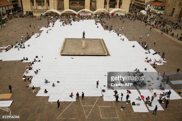 People sew white cloths with names of victims of the Colombian conflict painted in ash, at the Bolivar square in Bogota, on October 11, 2016....