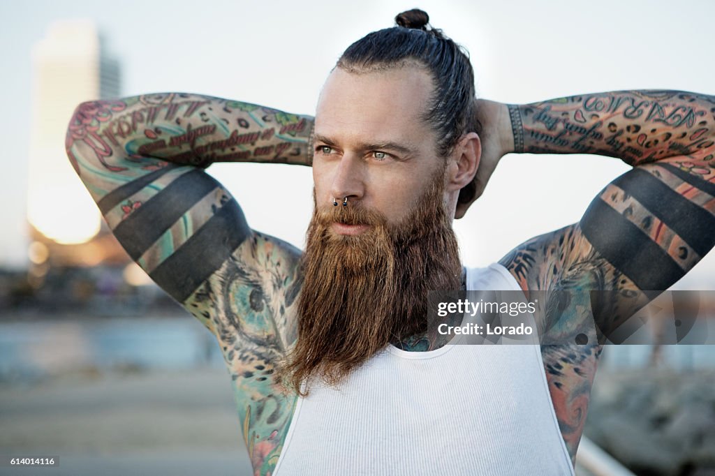 Heavily tattooed bearded athletic alternative man stretching before a workout