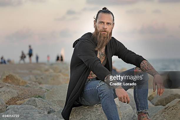 handsome bearded tattooed man sitting alone by the sea - tousled hair man stock pictures, royalty-free photos & images