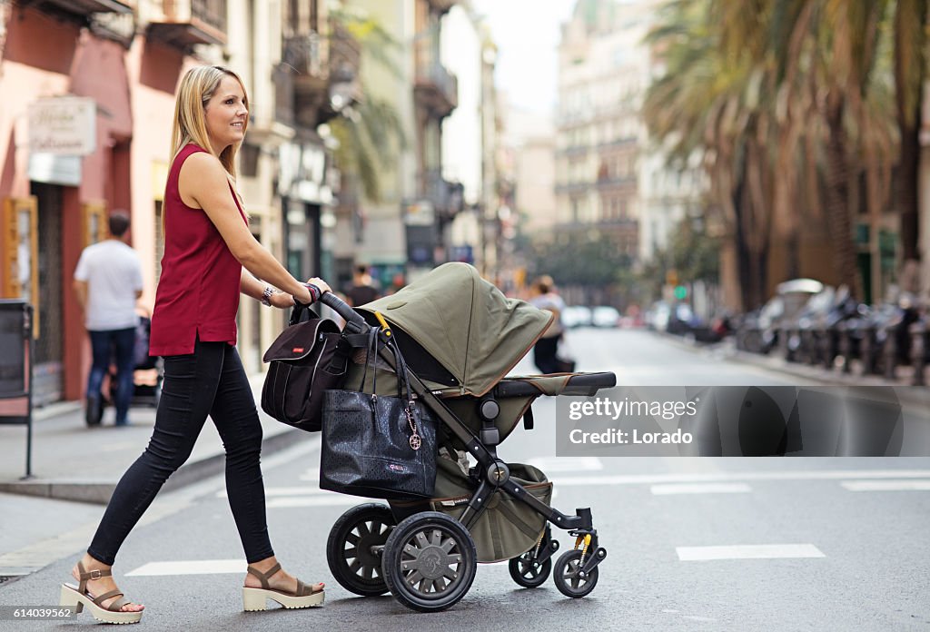 Pretty blonde mother walking in southern european city with pushchair