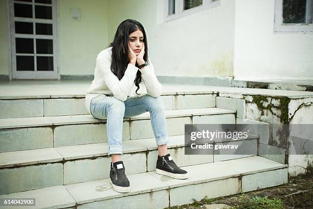 sad girl thinking and sitting on steps, holding her head. - zwart haar stockfoto's en -beelden