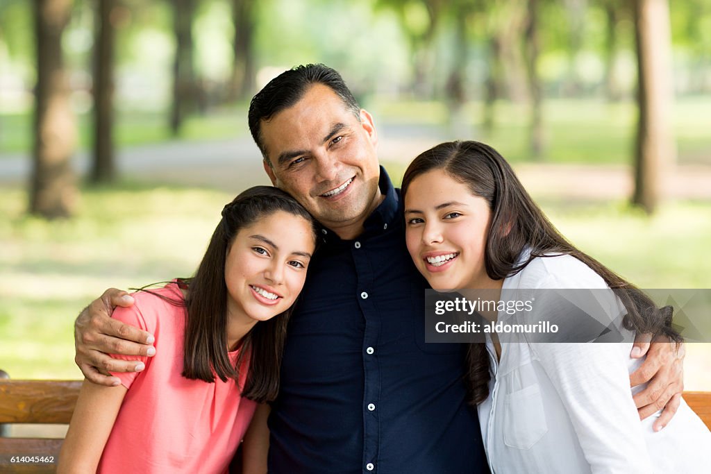 Latin father embracing his daughters and smiling at camera