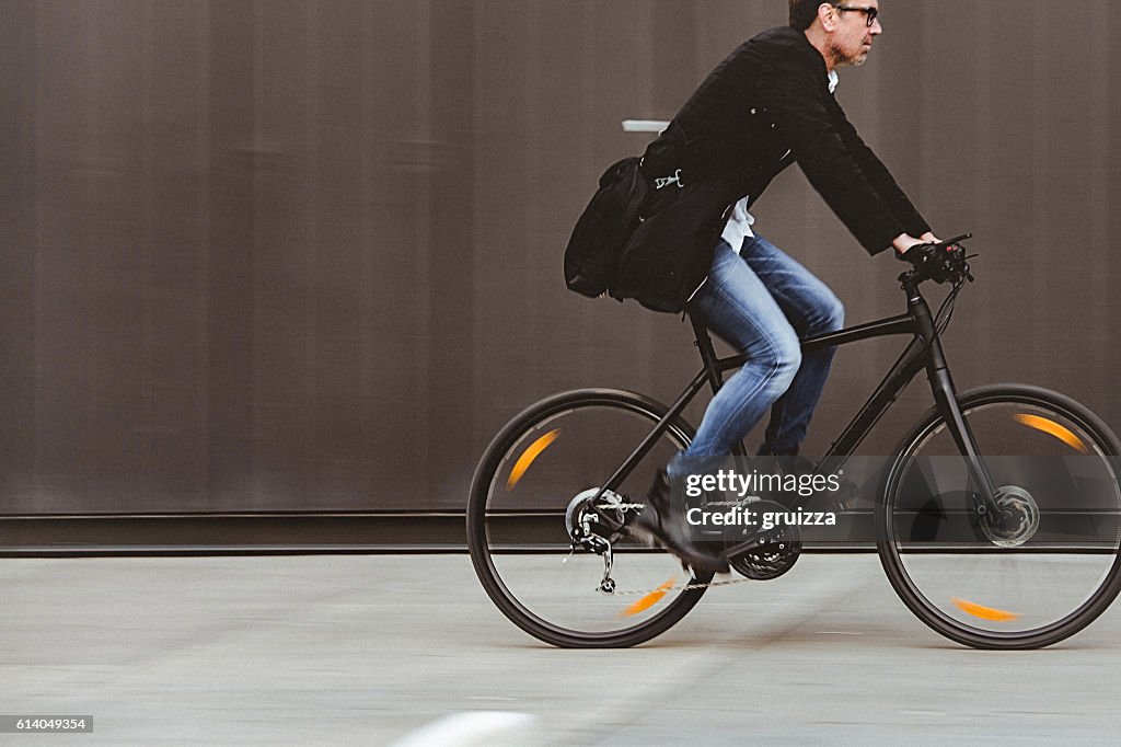 Handsome man riding bicycle beside the grey wall