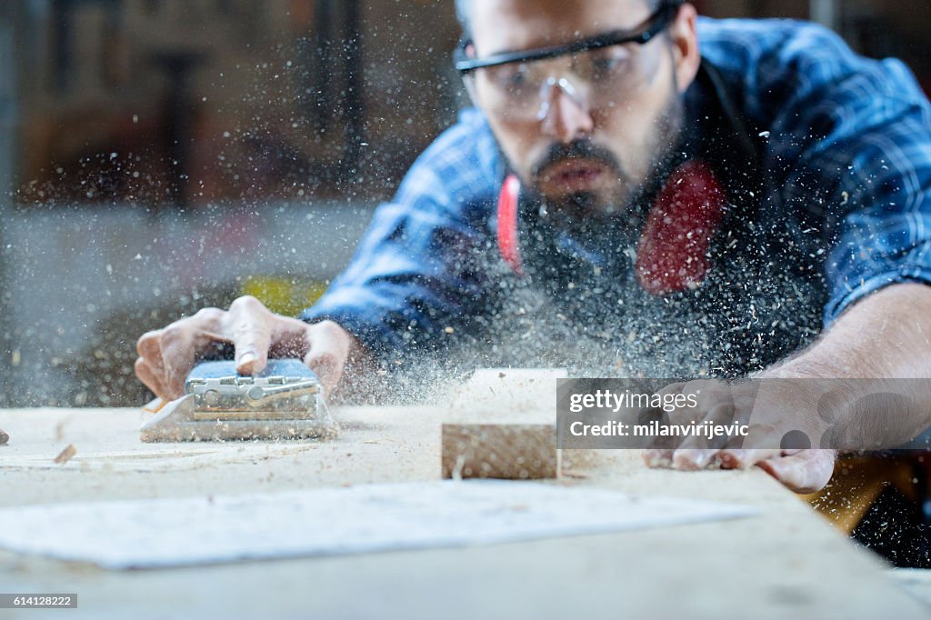 Young handosme carpenter blowing off sawdust
