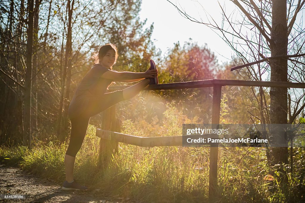 Young Woman Jogger Stretching Leg on Fence on Rural Path