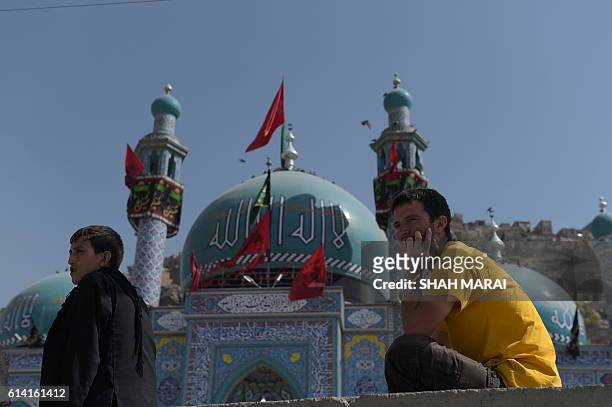 Two Afghan men sit in front of the Karte Sakhi shrine in Kabul on October 12 after an attack by gunmen late on October 11. Grieving worshippers on...